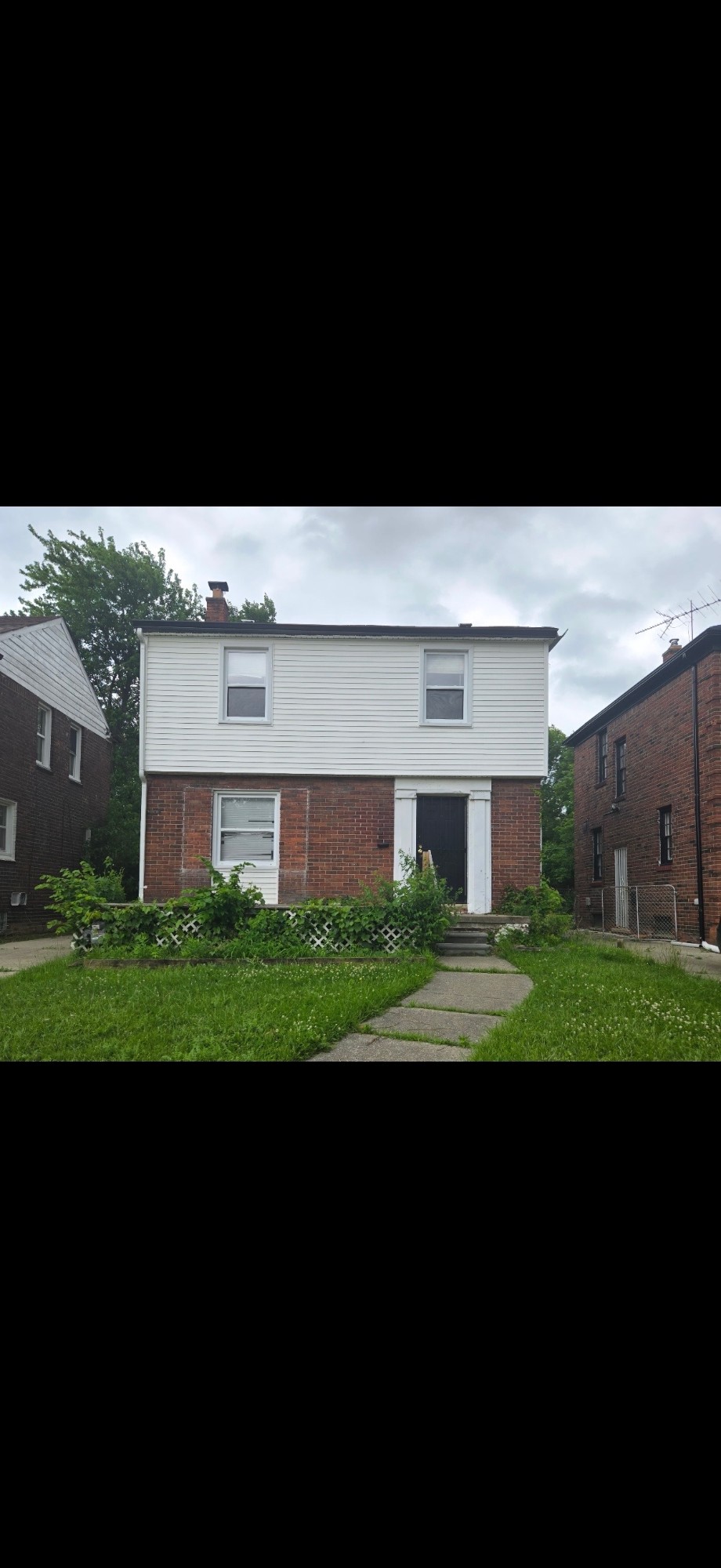 House exterior before renovation, overgrown lawn and worn siding