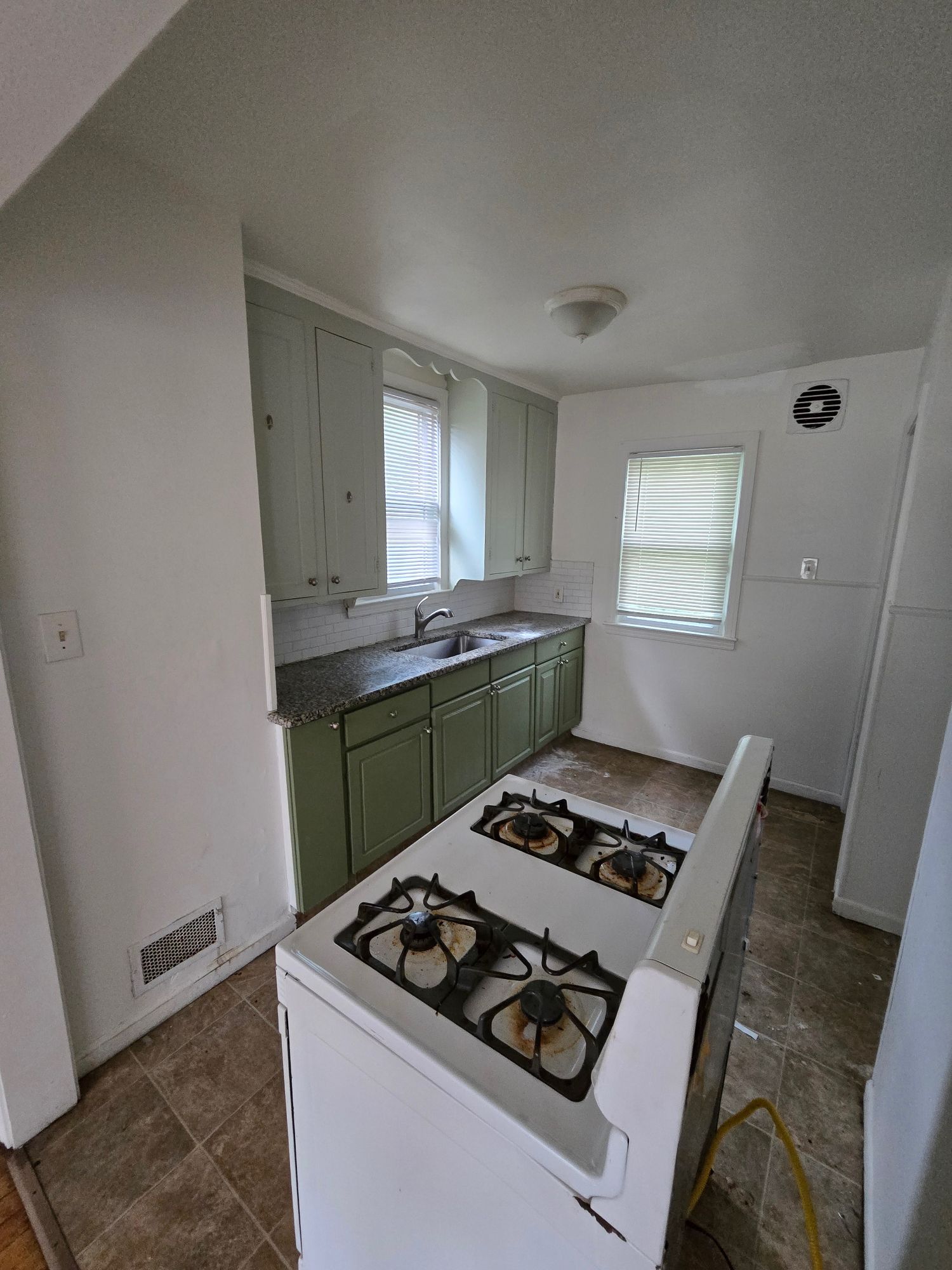 Kitchen before renovation with dated green cabinets and worn flooring